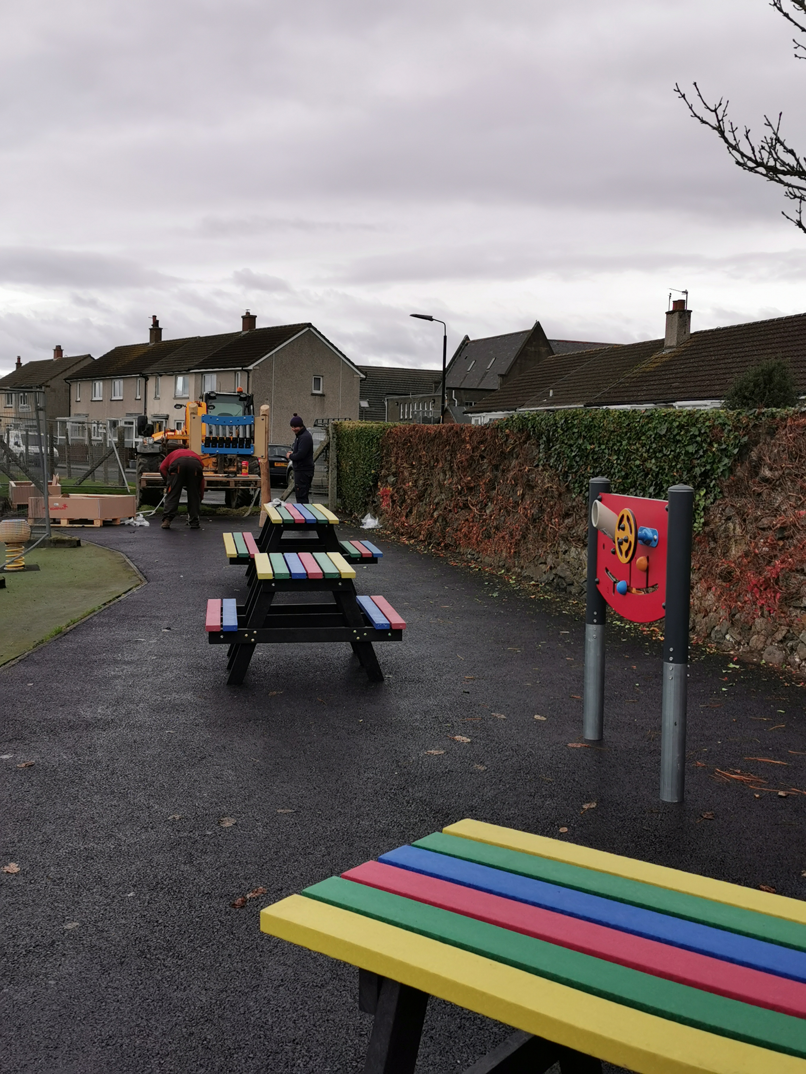 A picture of brightly coloured picnic benches and smooth surface next to a playpark.